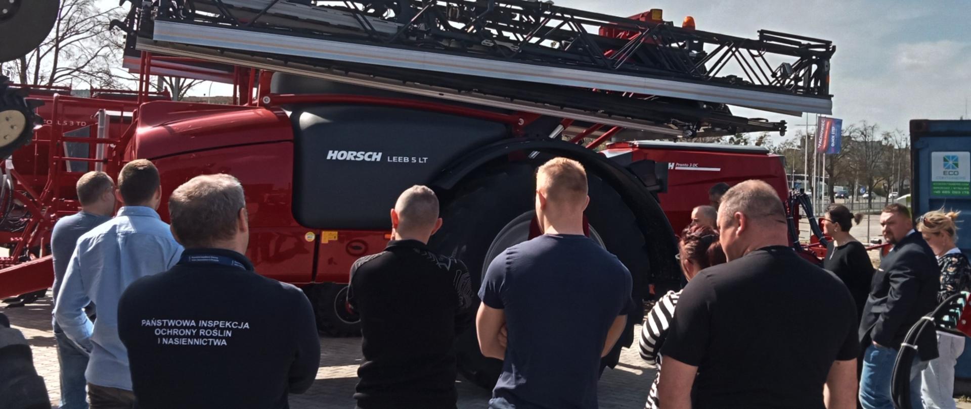 Mężczyźni w ciemnych ubraniach oglądają czerwoną maszynę rolniczą