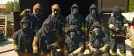 Grupa strażaków w ubraniach specjalnych z sprzętem ochrony układu oddechowego na tle komory ogniowej