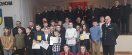 W sali gminnego ośrodka kultury stoją zwycięzcy eliminacji powiatowych OTWP. Dzieci trzymają w rękach nagrody oraz dyplomy. Za nimi stoją przedstawiciele władz oraz Komendant Powiatowy PSP w Bytowie
