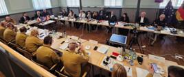 Uczestnicy 5. Polsko-Niemieckiego Forum Komendantów Straży Pożarnych podczas obrad przy wspólnym stole, z widocznymi flagami Polski, Niemiec i UE.