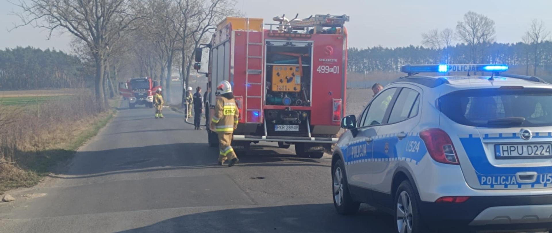 Zdjęcie przedstawia strażaków gaszących trawę - na zdjęciu pojazdy służb