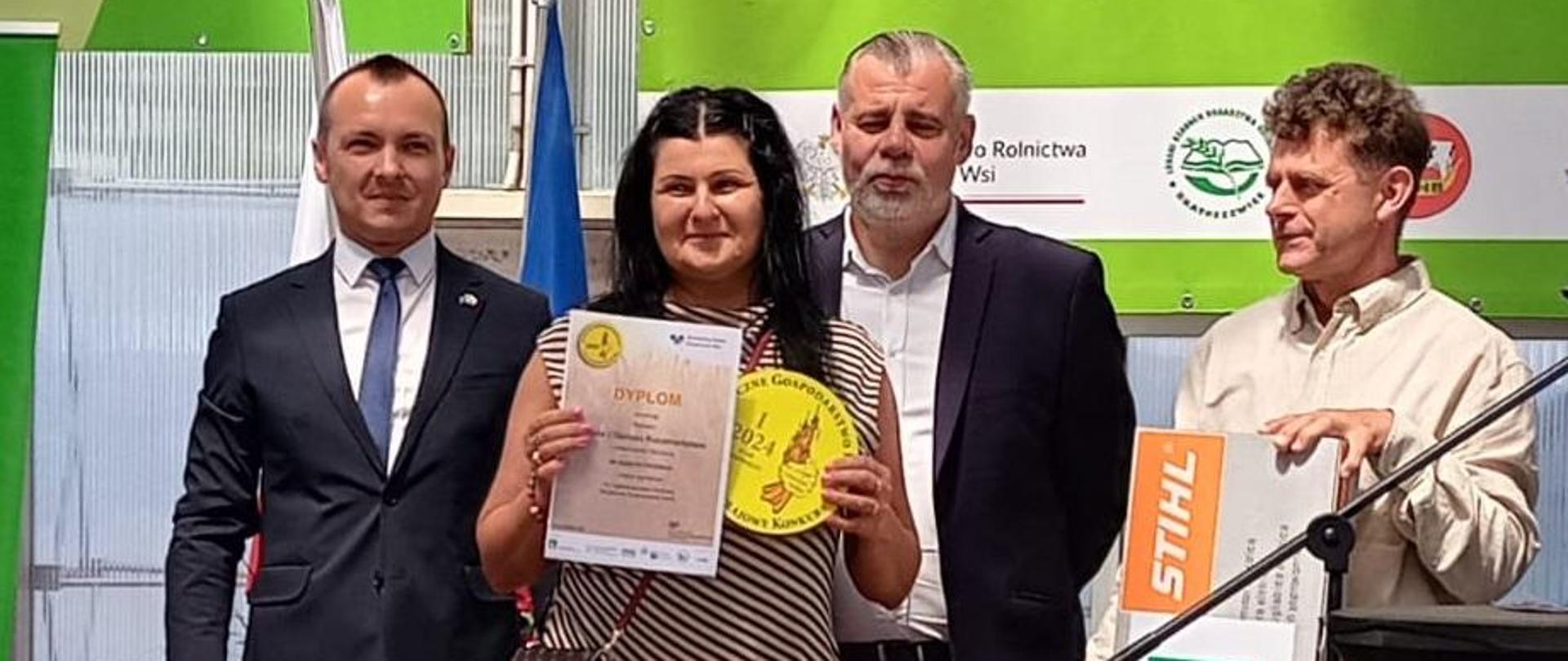 Kobieta trzyma w ręce dyplom z logo BGR i KRUS, obok stoi trzech mężczyzn.