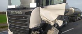 Wypadek na obwodnicy Rawicza. Na pierwszym planie samochód ciężarowy - cysterna do przewozu mleka raz z przyczepą - także cysterną. Kabina pojazdu jest koloru białego. Otwarte są drzwi od strony kierowcy. Pojazd ma uszkodzoną przednia - lewą część (łącznie z zawieszeniem). 