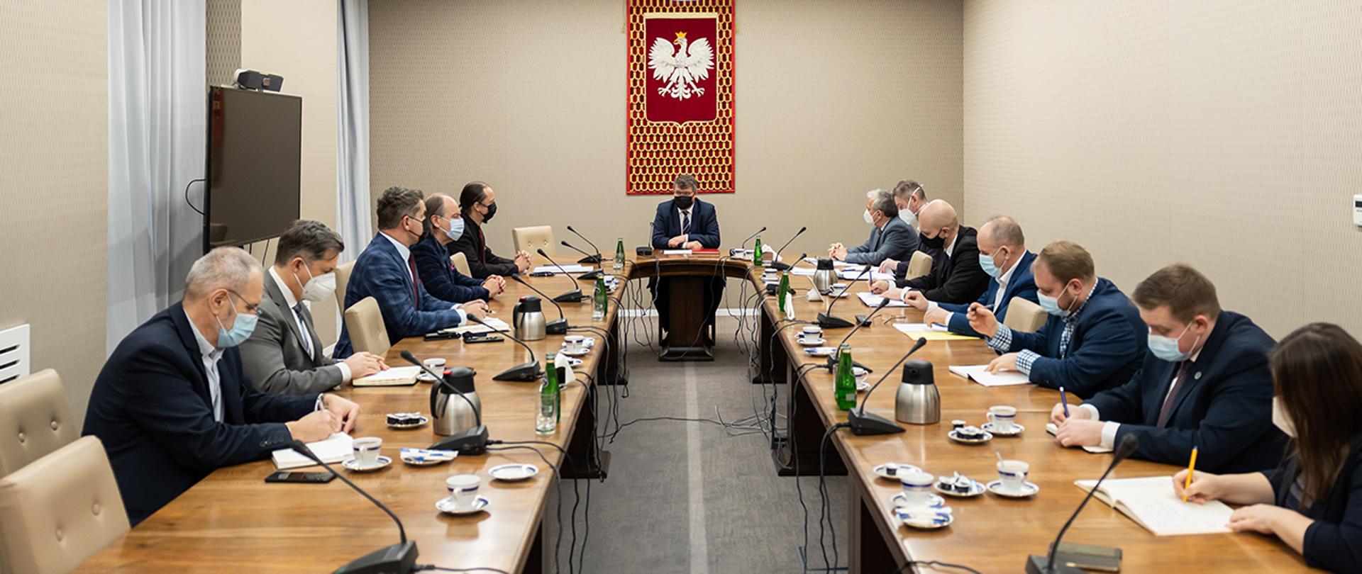 Wiceminister Maciej Wąsik oraz przedstawiciele związków zawodowych służb mundurowych podległych MSWiA podczas rozmowy przy wspólnym stole.