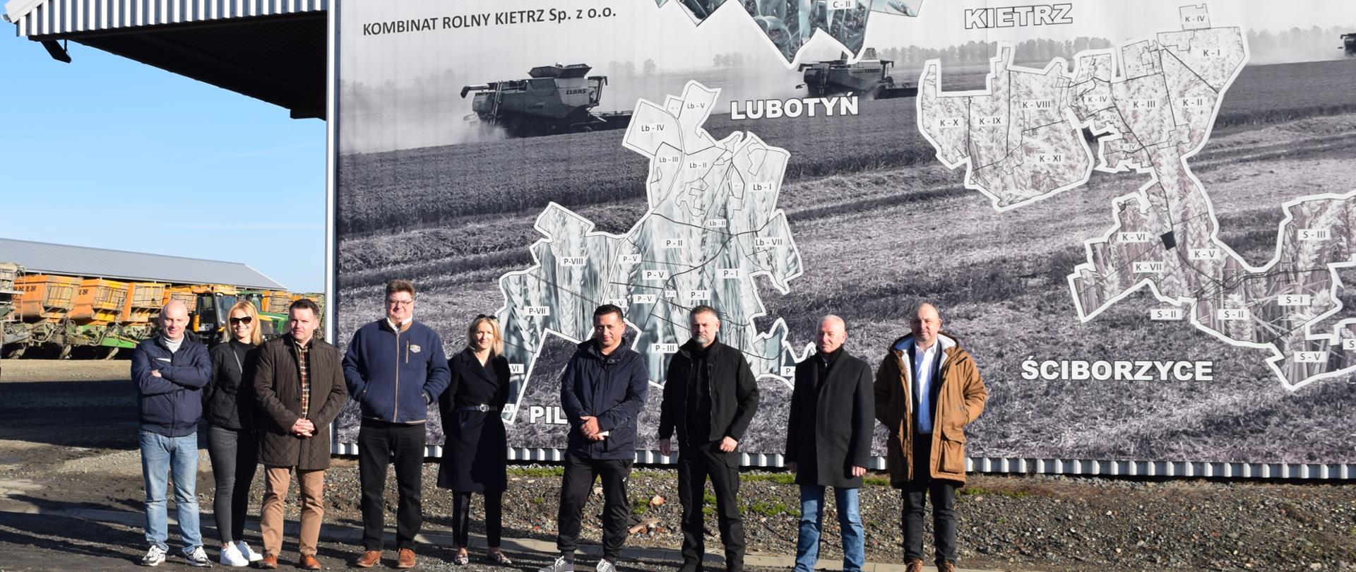 Uczestnicy wizyty w Kombinacie Rolnym Kietrz. W tle mural na ścianie budynku. 