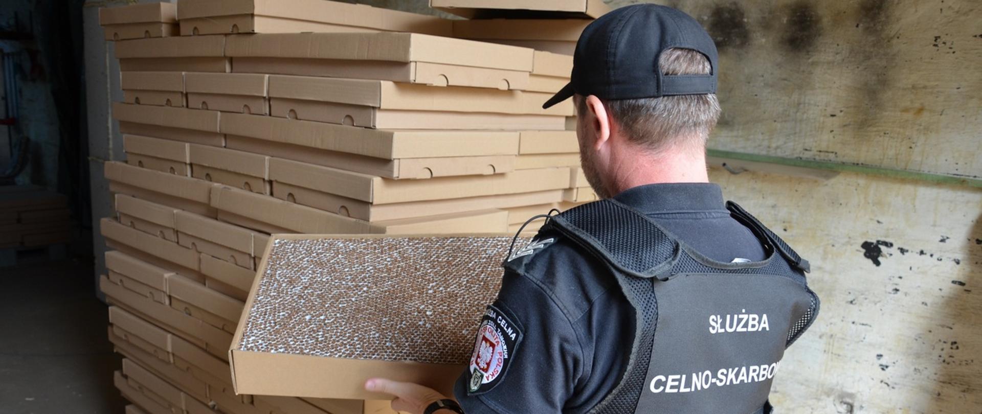 Funkcjonariusz KAS trzyma karton z nielegalnymi papierosami