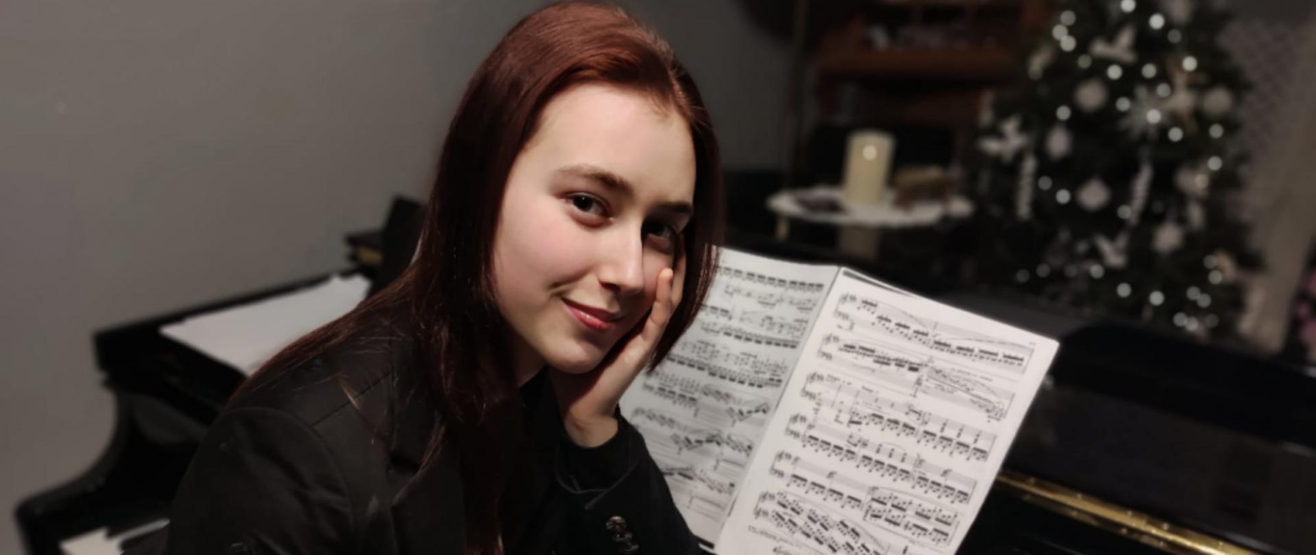 Młoda dziewczyna siedzi przy fortepianie. Na pulpicie stoją nuty.