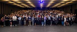 Zdjęcie zbiorowe, w wielkiej sali stoi duża grupa kilkuset osób.