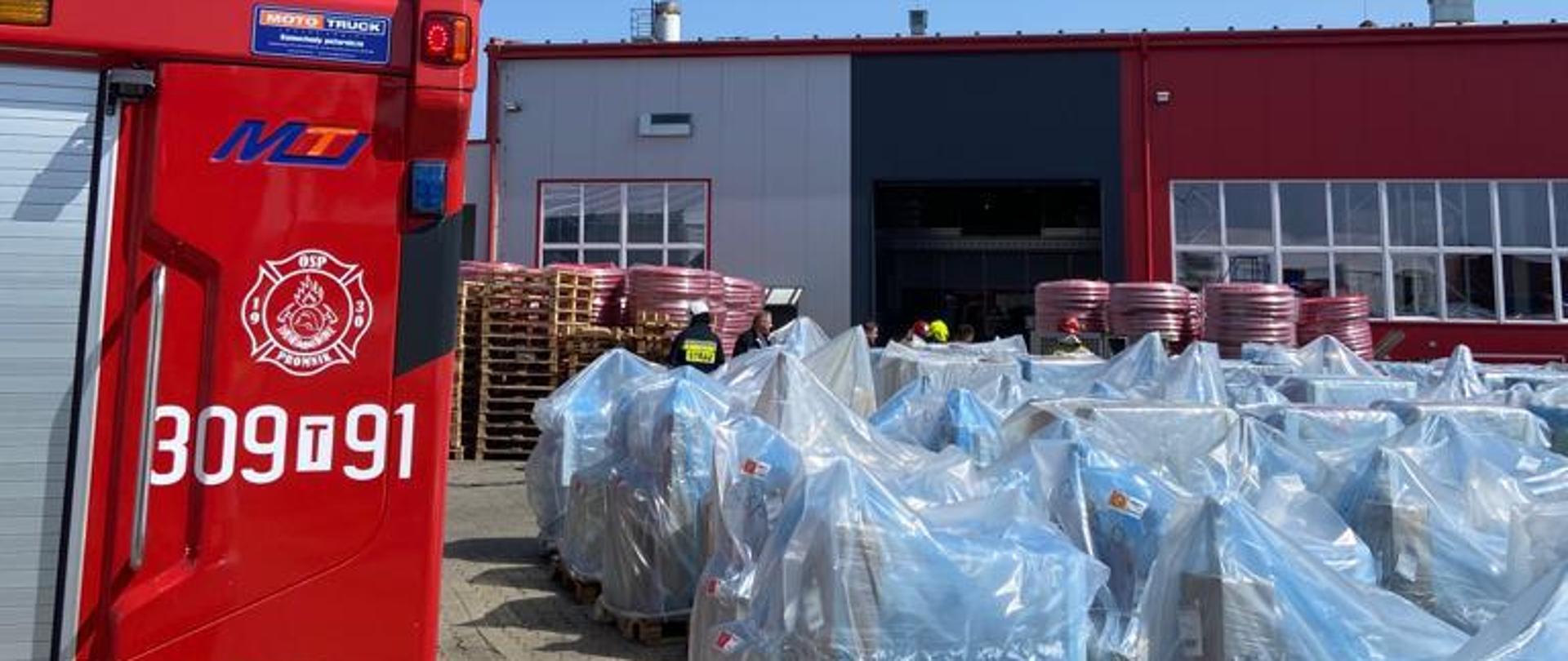 Na zdjęciu widać z lewej strony wóz pożarniczy a po prawej halę produkcyjną. Bliżej stoją zapakowane nowe urządzenia do sprzedaży.