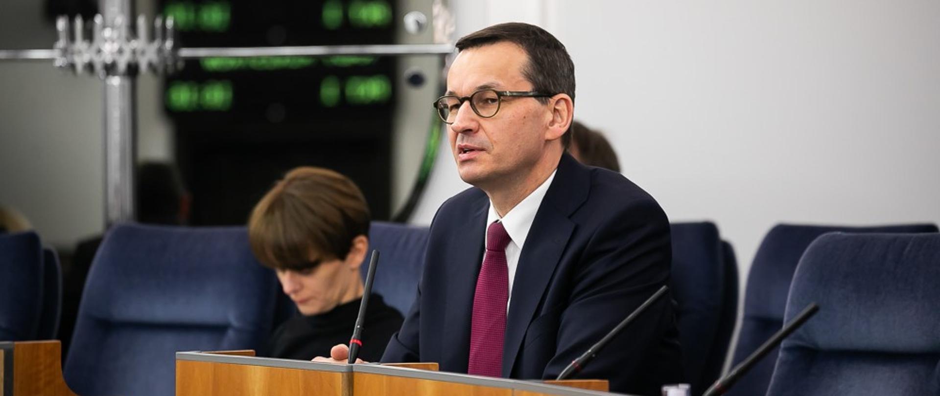 Premier Mateusz Morawiecki siedzi podczas wypowiedzi w senacie.