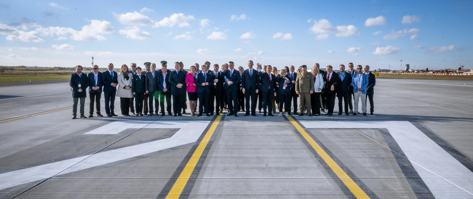 Zdjęcie przedstawia grupę osób pa drodze lotniskowej