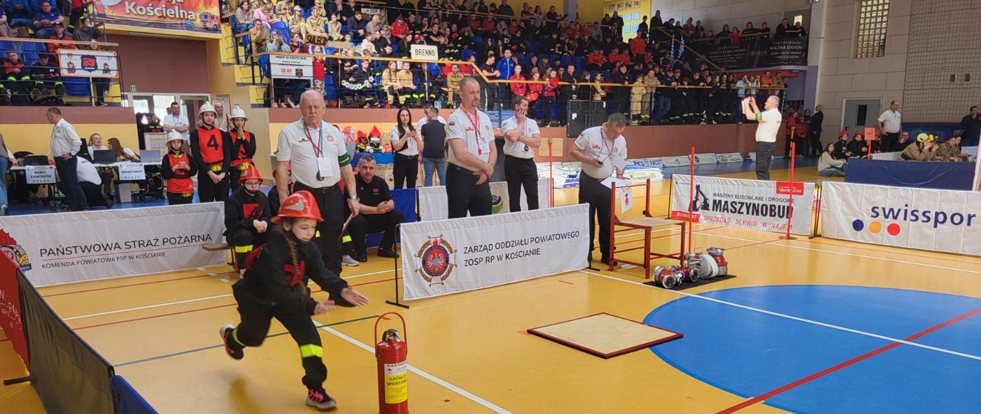 Strażacy podczas wykonywania ćwiczeń na torze. Na trybunach siedzą widzowie, strażacy czekający na swój start. Strażacy podczas dekoracji, z włodarzami i przedstawicielami instytucji.