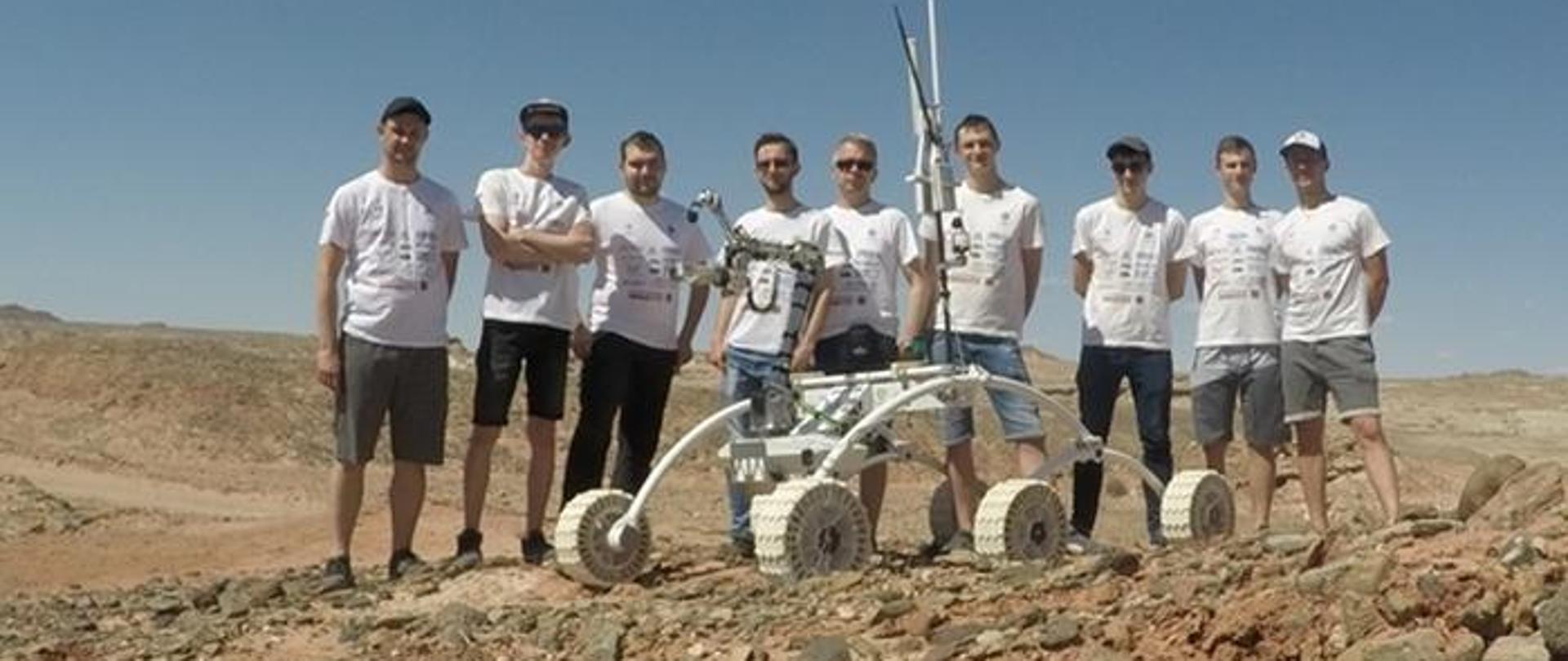 Grupa ludzi na pustyni, przed nimi łazik