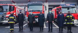 Zdjęcie przedstawia funkcjonariuszy Państwowej Straży Pożarnej na tle pojazdów pożarniczych stojących przed obiektem Komendy Miejskiej Państwowej Straży Pożarnej w Częstochowie