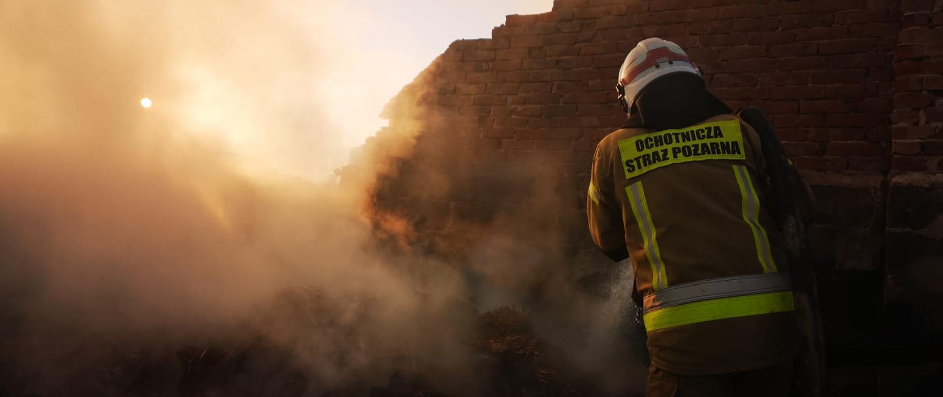 Widoczne miejsce zdarzenia widać dym i strażaka prowadzącego działania gaśnicze.