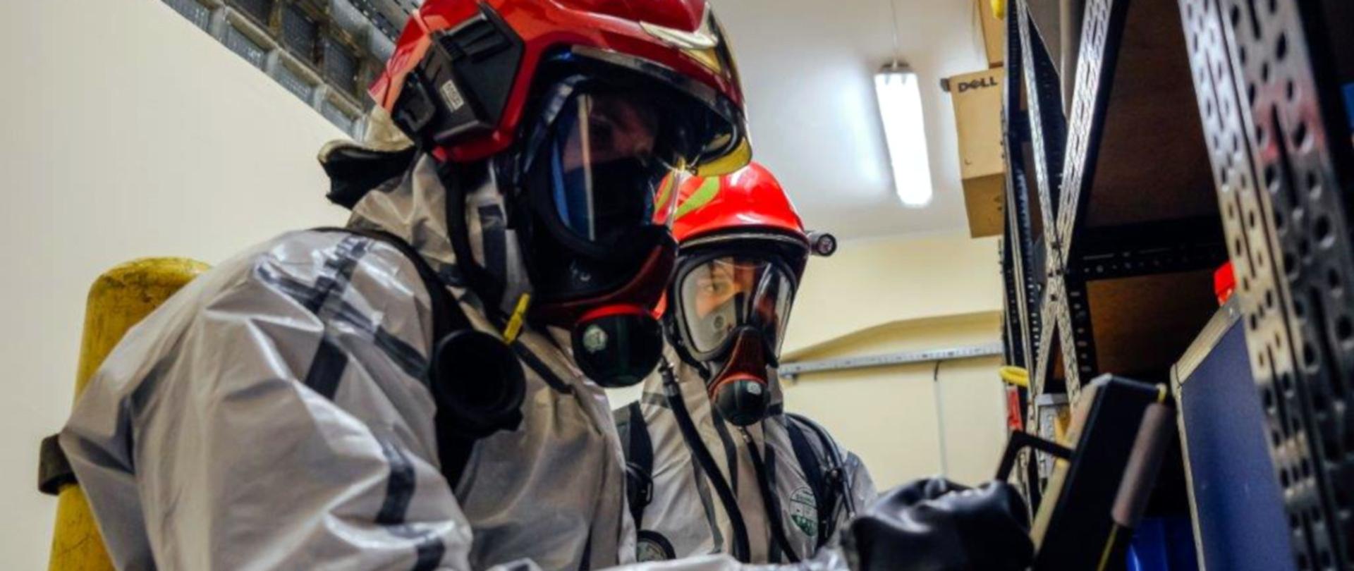 Na zdjęciu dwóch strażaków w na plecach mają butle powietrzne, na twarzy maski powietrzne 