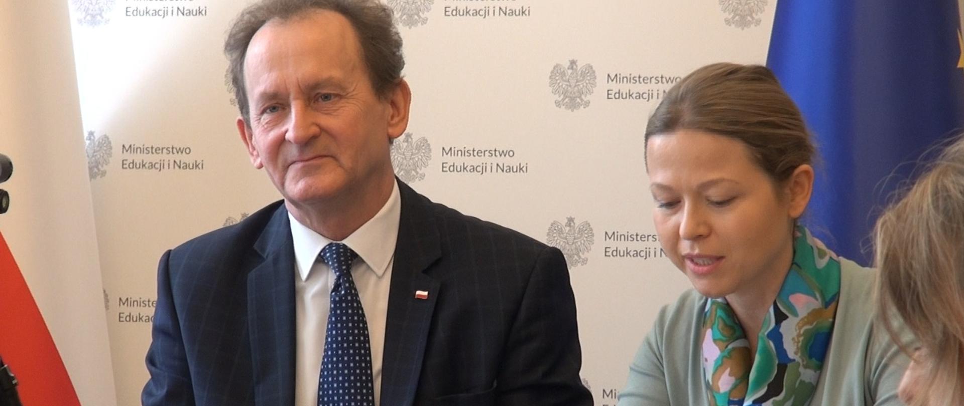 III Polsko-Brytyjskie Forum Naukowe z udziałem wiceministra Włodzimierza Bernackiego, wiceminister Włodzimierz Bernacki siedzi w towarzystwie uczestniczki forum, z tyłu znajduje się baner Ministerstwa Edukacji i Nauki.