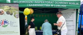 Pracownica Wojewódzkiego Inspektoratu Ochrony Roślin i Nasiennictwa w Lublinie na stoisku podczas prezentuje interesantom materiały informacyjne na tle namiotu i stojaków reklamowych