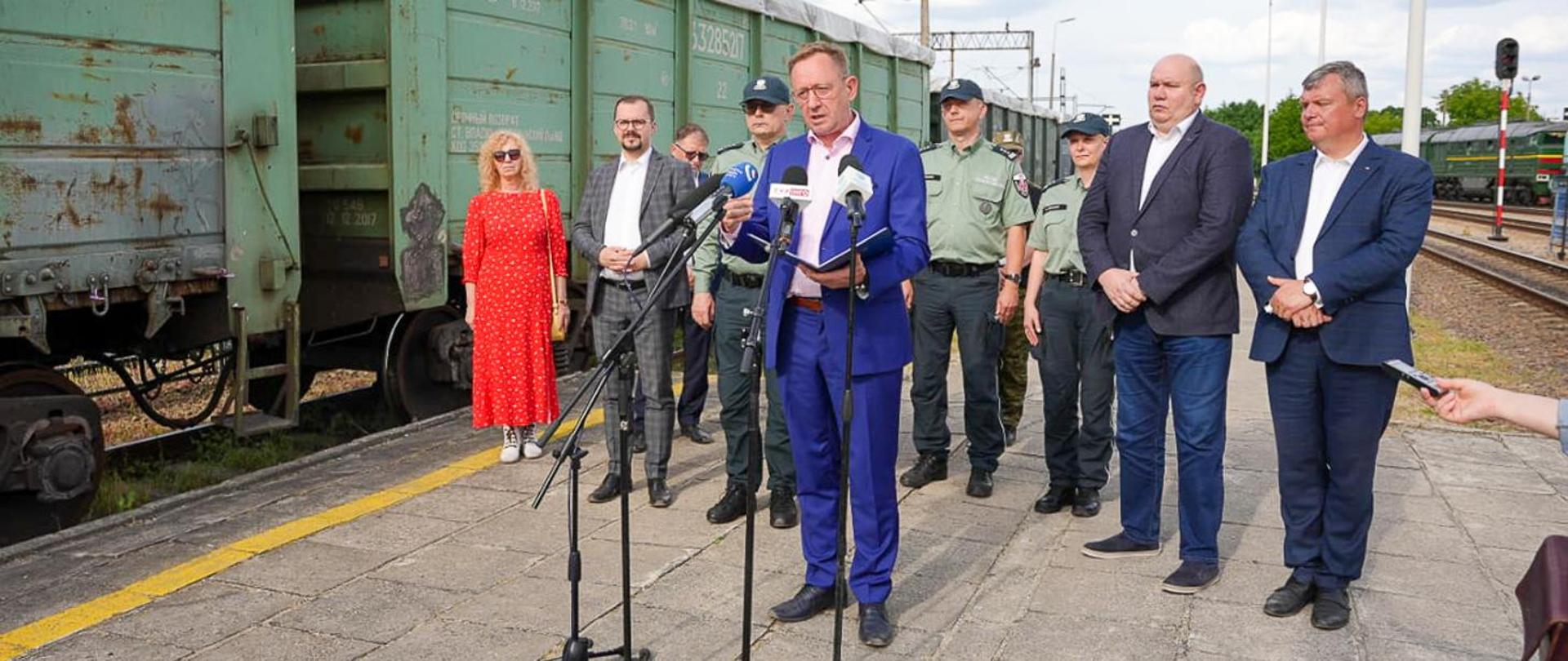 Minister rolnictwa stoi przed mikrofonem. Za nim pozostali uczestnicy spotkania. 