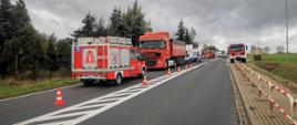 Na zdjęciu na jednym pasie drogi stoi samochód ratowniczo - gaśniczy za nim pojazd ciezarowy i dostawczy uczestnicy kolizji dalej ZRM i za nim samochód ratowniczo - gaśniczy po drugiej stronie stoi samochód ratowniczo - gaśniczy przy przystanku miejsce prowadzenia działań oddzielone pachołkami 