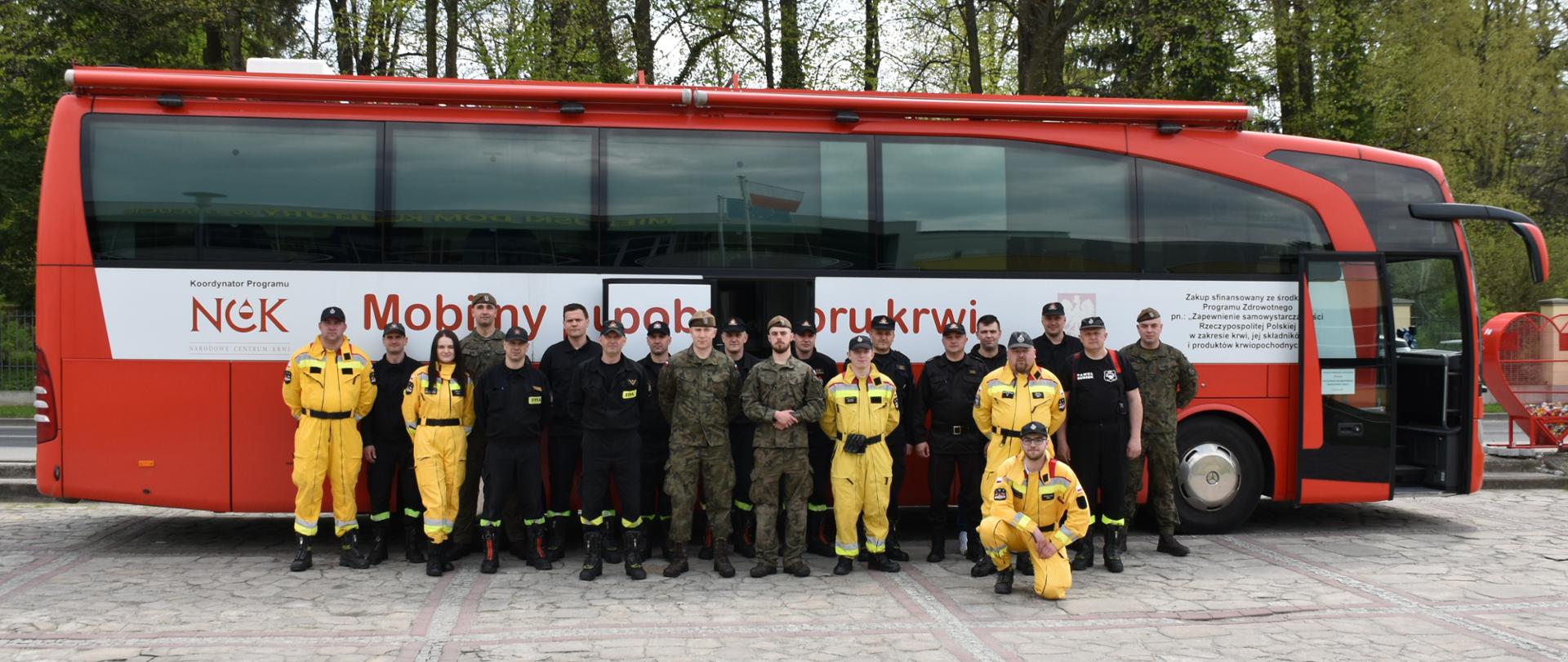 Na zdjęciu autobus regionalnego centrum krwiodawstwa. Przed autokarem stoją w umundurowaniach koszarowych strażacy Państwowej Straży Pożarnej w Łańcucie, Strażacy z Ochotniczej Straży Pożarnej w Husowie, oraz żołnierze 3 podkarpackiej brygady obrony terytorialnej.