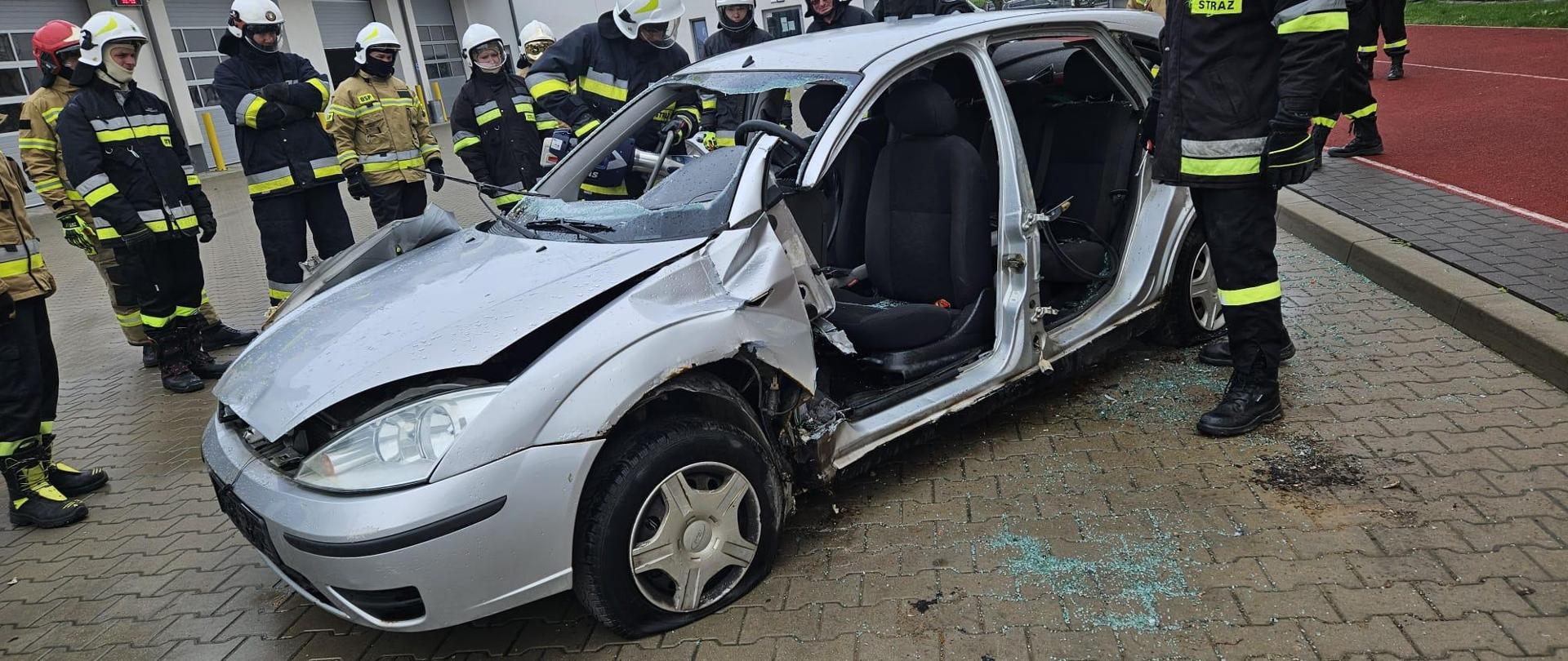 Strażacy stoją przy pociętym samochodzie na placu KM PSP w Suwałkach