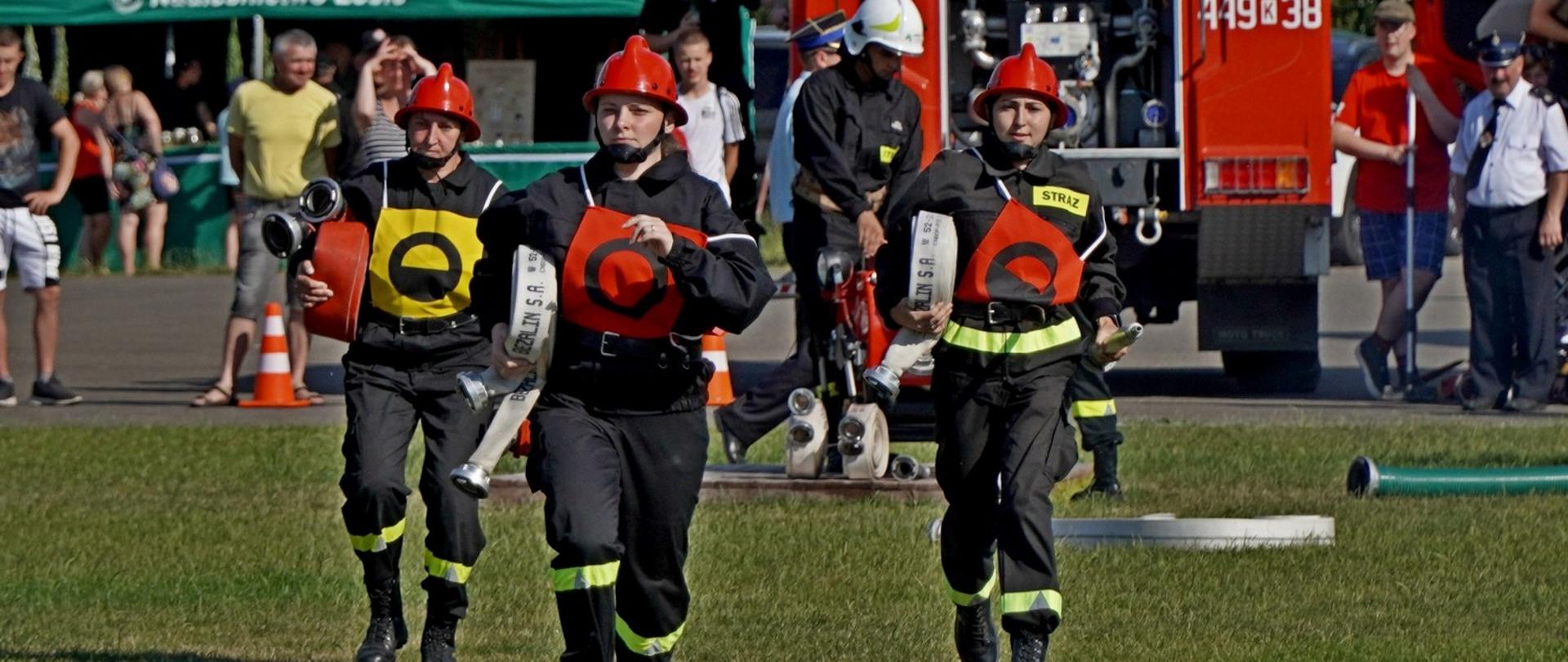 Na zdjęciu widoczni strażacy ochotnicy w ubraniach koszarowych rozwijający linie gaśnicze podczas XI Powiatowych Zawodów Sportowo - Pożarniczych na stadionie w Uściu Gorlickim podczas konkurencji ćwiczenie bojowe.