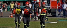 Na zdjęciu widoczni strażacy ochotnicy w ubraniach koszarowych rozwijający linie gaśnicze podczas XI Powiatowych Zawodów Sportowo - Pożarniczych na stadionie w Uściu Gorlickim podczas konkurencji ćwiczenie bojowe.