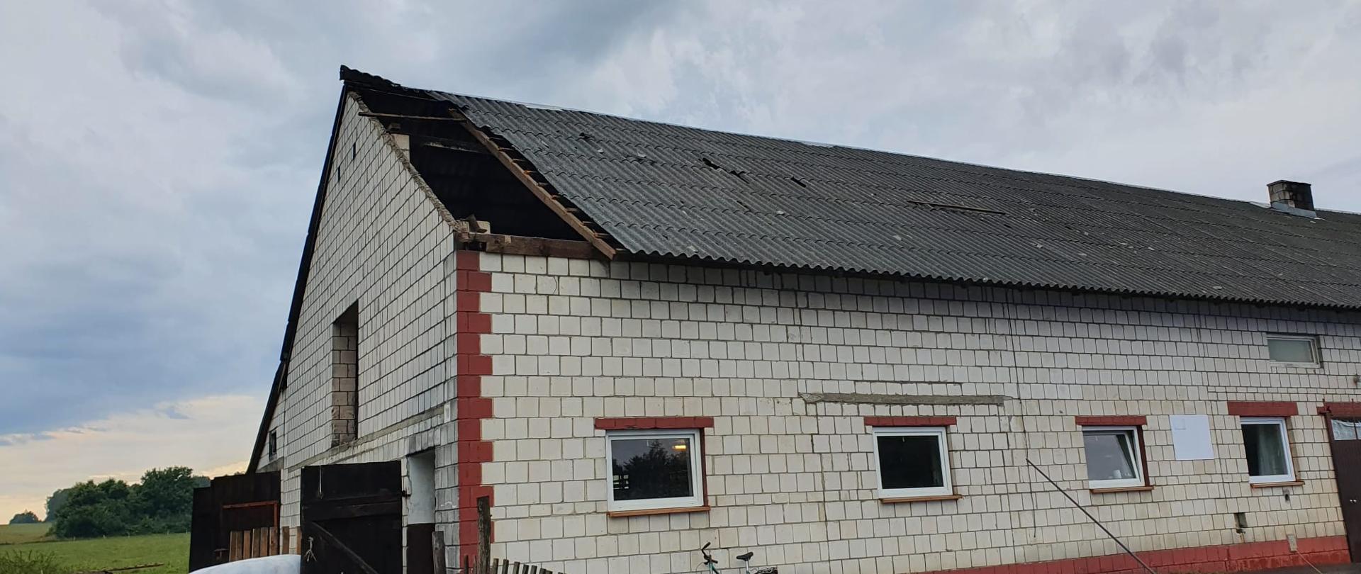 Zdjęcie przedstawia uszkodzony dach z eternitu na budynku gospodarczym.