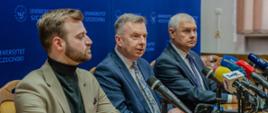 Minister Wieczorek i dwóch mężczyzn w garniturach siedzą za drewnianym stołem, za nimi niebieska ścianka z napisem Uniwersytet Szczeciński.