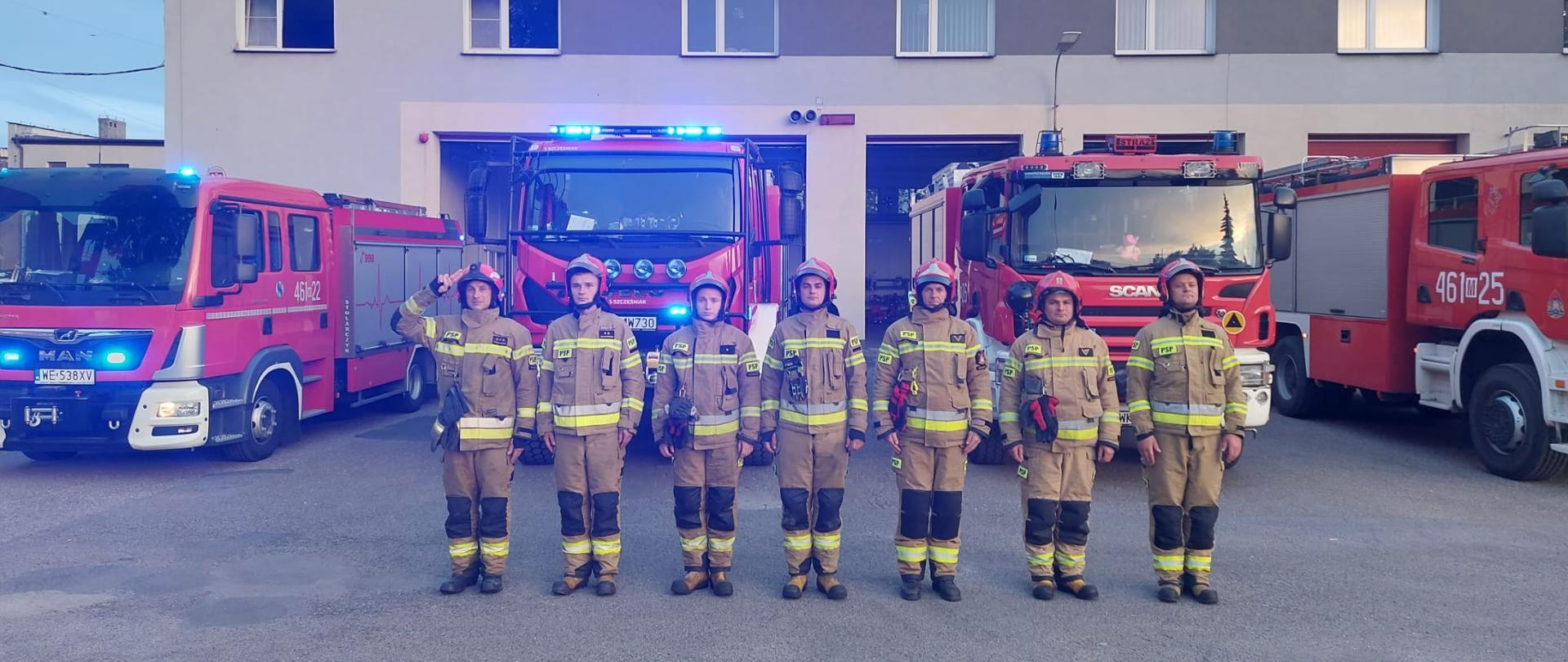 strażacy oddający Hołd Druhowi OSP Balice na placu komendy, w tle samochody pożarnicze z włączonymi światłami