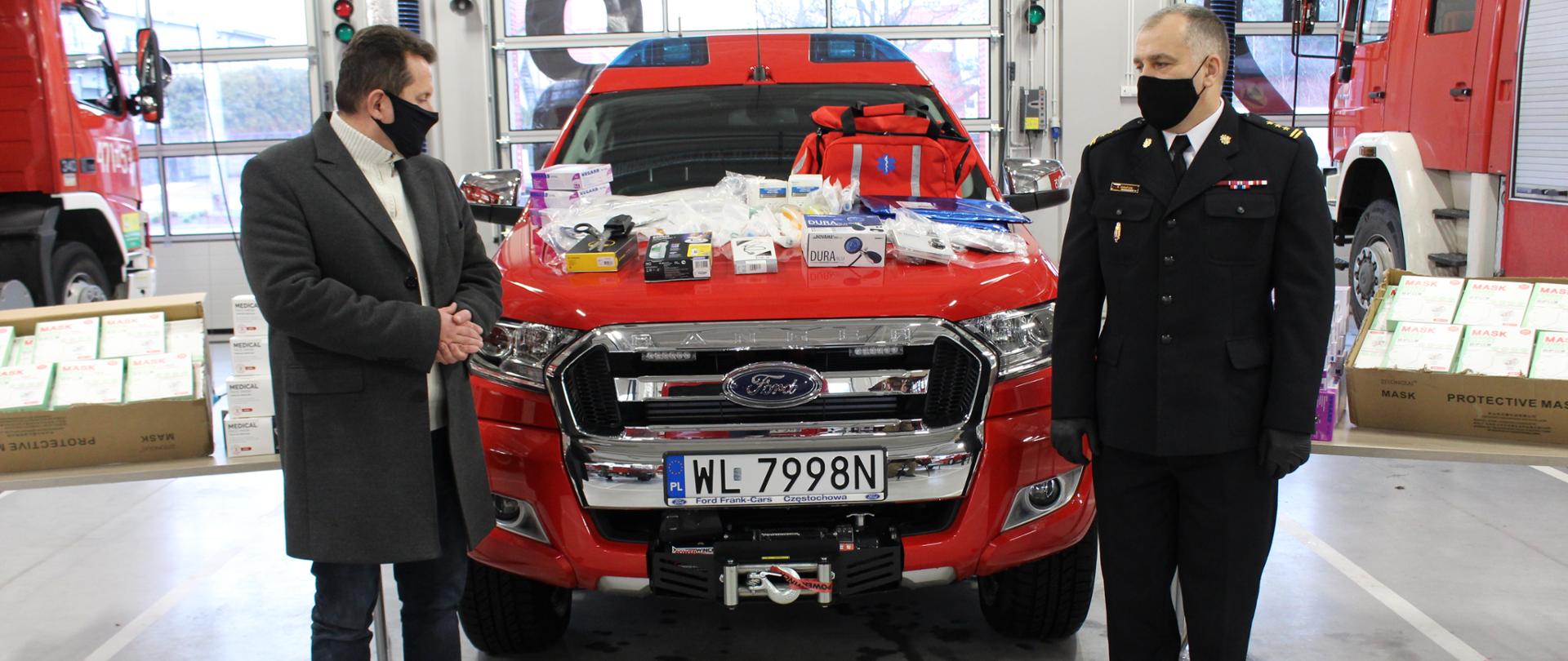 Przekazanie sprzętu medycznego i środków ochrony indywidualnej dla KP PSP w Legionowie. na środku zdjęcia samochód strażacki czerwony. Na masce samochodu leża środki medyczne oraz torba medyczna.
Na zdjęciu widać 2 osoby po lewej Prezydent miasta Legionowo Roman Smogorzewski po prawej w mundurze Komendant Powiatowy PSP w Legionowie st. bryg. Radosław Parapura. 