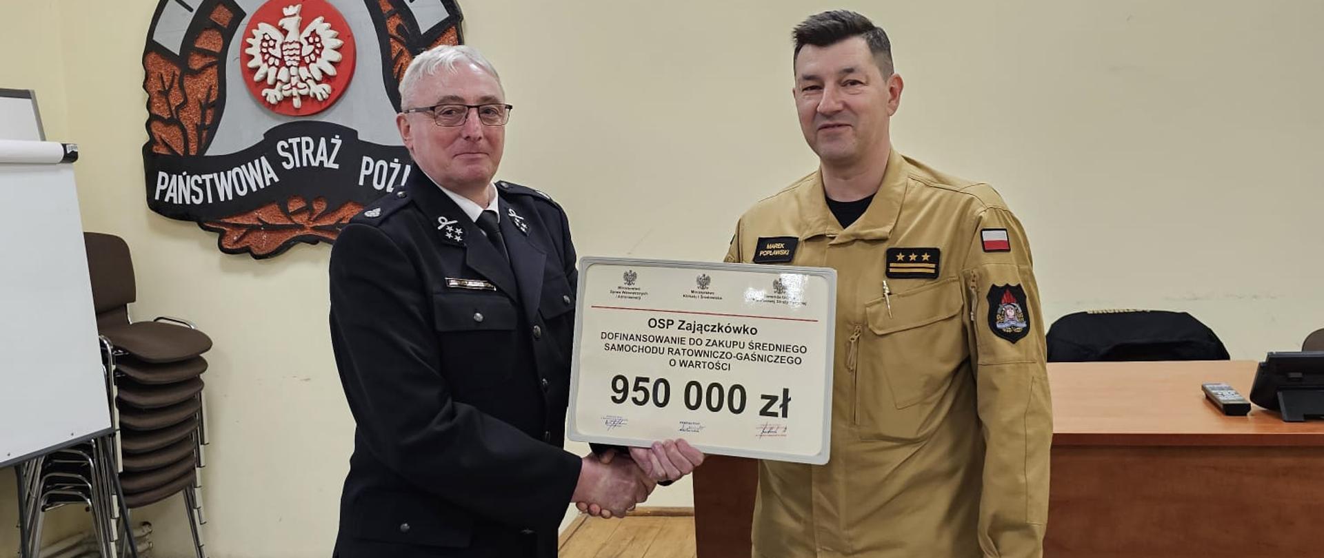 Zdjęcie przedstawia moment wręczenia Promesa dla OSP Zajączkówko. Na zdjęciu znajduje się dwóch mężczyzn.