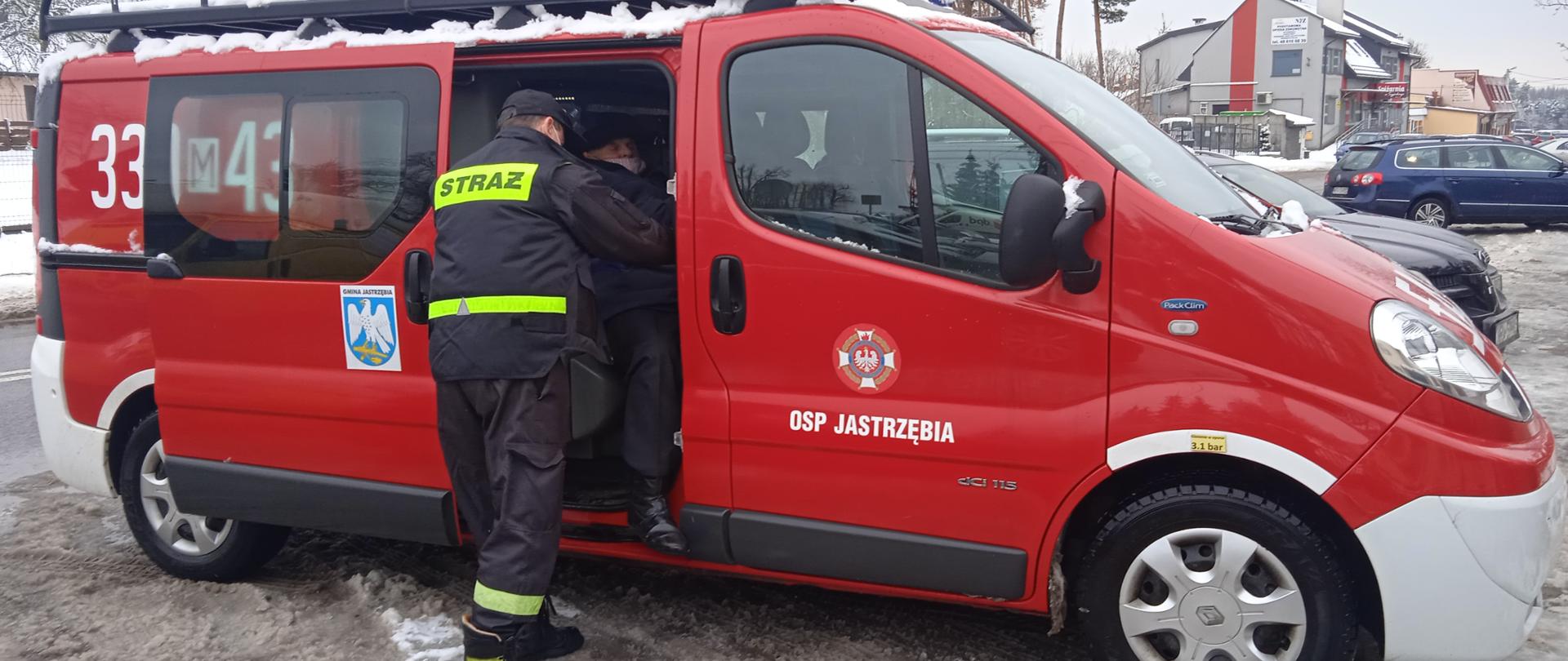 Strażak pomaga osobie starszej wysiąść z samochodu pożarniczego typu bus