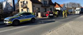 Na zdjęciu widać samochód osobowy na chodniku, patrol Policji i strażaków podczas prowadzenia działań ratowniczych.