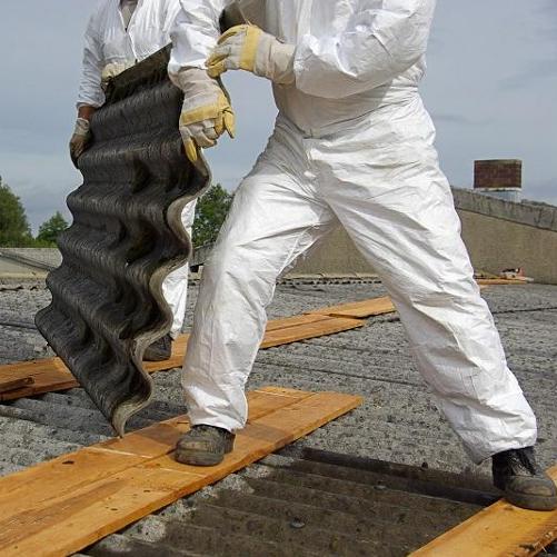 Mężczyźni w ochronnych kombinezonach i rękawicach usuwają płyty eternitu z dachu