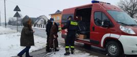 Strażacy prowadzą starszą osobę do samochodu pożarniczego na transport przeciw COVID-19