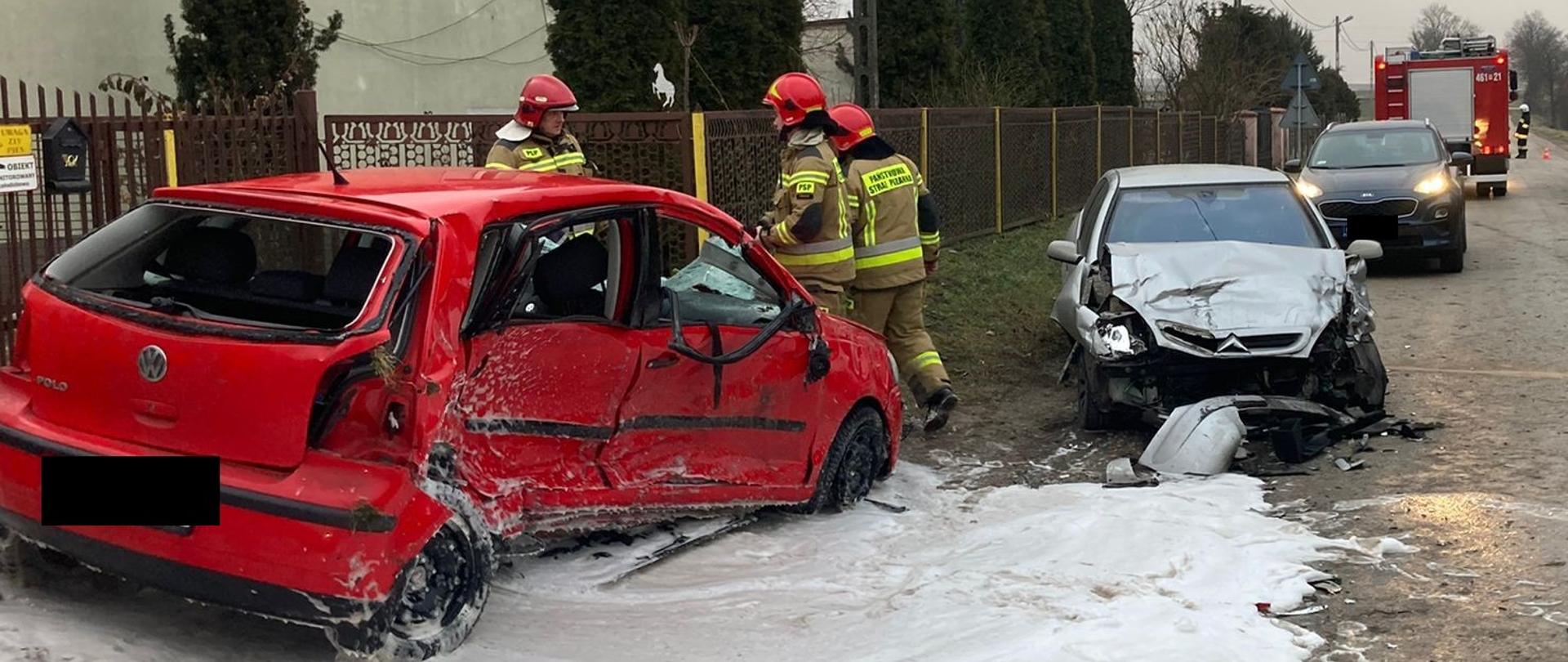 Zdjęcie przedstawia strażaków prowadzących działania ratownicze w obrębie wraku pojazdu Vw Polo. W Tle widać wrak Citroena Xara i średni samochód pożarniczy. 