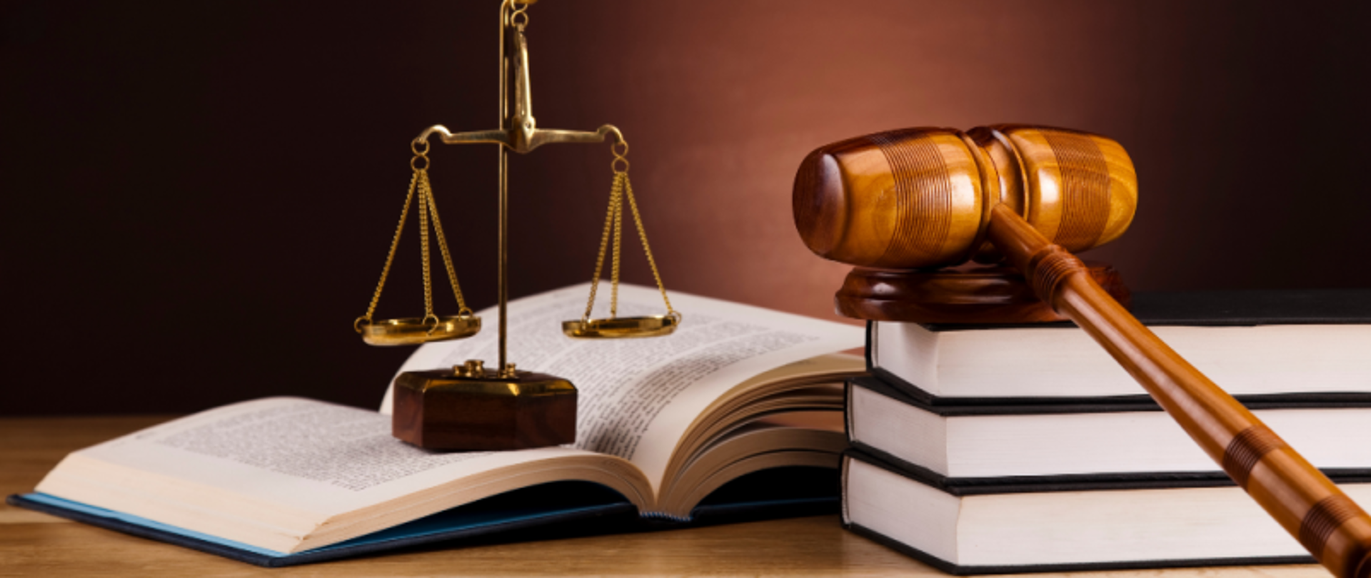 Blat biurka. Na nim leżą książki, młotek sędziowski na podstawce i ozdobna waga.