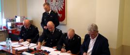 Zdjęcie przedstawia przedstawicieli straży państwowej i osp oraz władze miasta podpisujących dokumenty w biurze. 