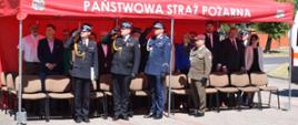 Na zdjęciu widać trybunę honorową w której znajdują się zaproszeniu goście. W pierwszym rzędzie kolejno Komendant Powiatowy Straży Pożarnej w Rawie Mazowieckiej, Zastępca Komendanta Wojewódzkiego Państwowej Straży Pożarnej w Łodzi, Komendant Powiatowy Policji w Rawie Mazowieckiej oraz Szef Wojskowego Centrum Rekrutacji w Skierniewicach.