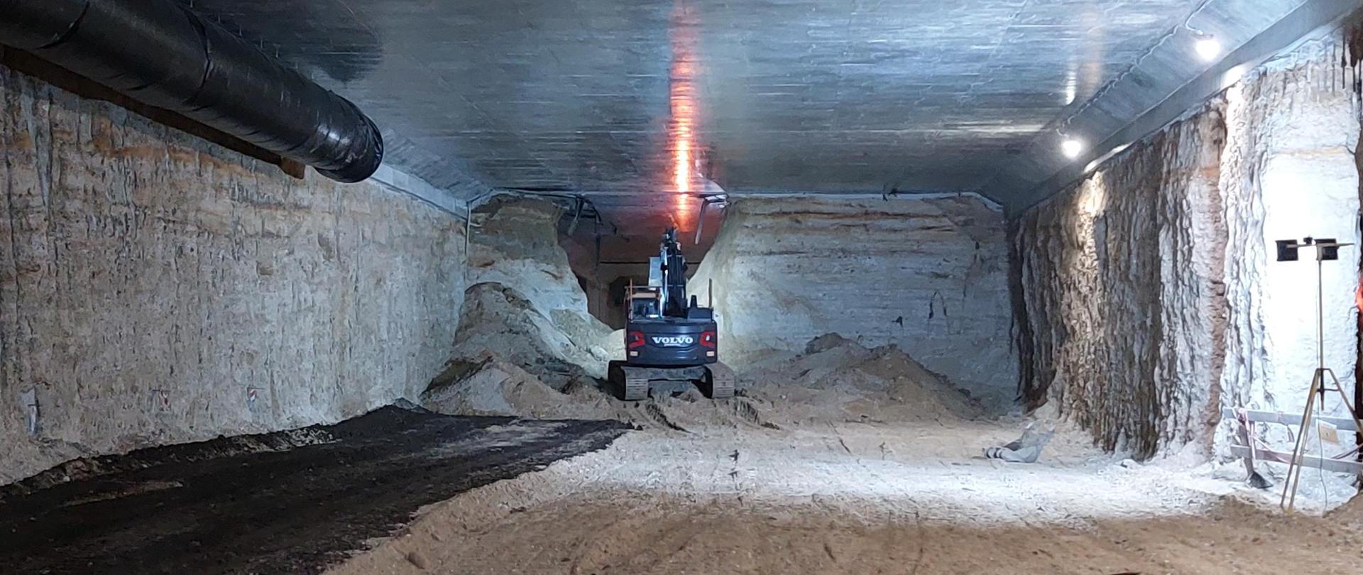Zdjęcie wykonane we wnętrzu budowanego tunelu na S52, południowej obwodnicy Krakowa. Maszyna budowlana (koparka) usuwa ostatnią warstwę ziemi aby połączyć obie wykopane części tunelu.