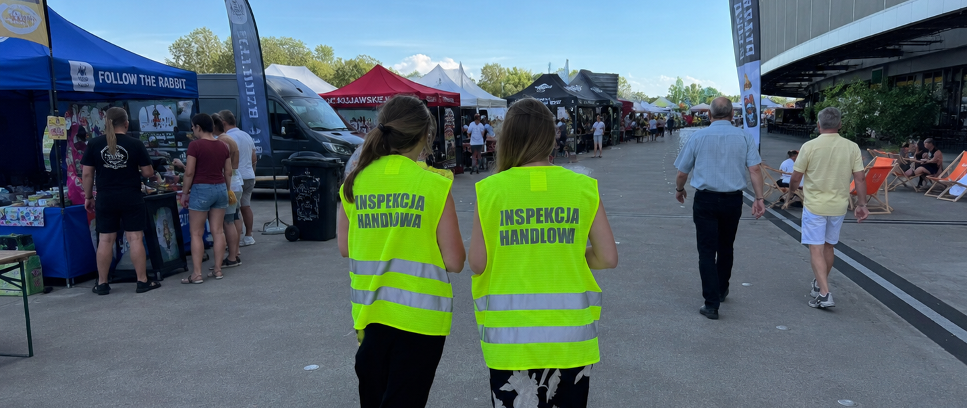 Na pierwszym planie dwie inspektorki Inspekcji Handlowej. W tle namioty przedsiębiorców rozstawione na płycie przy stadionie w trakcie festiwalu.