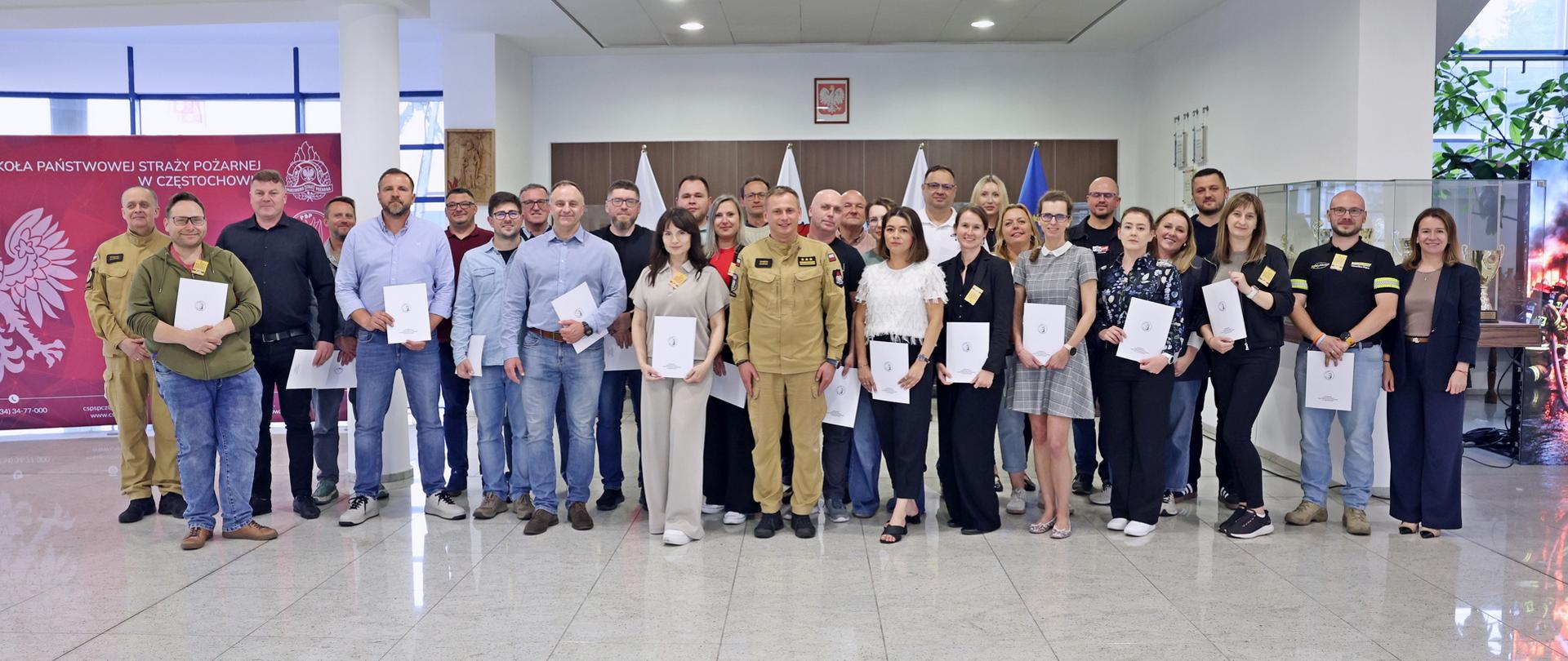 Pamiątkowe zdjęcie grupowe uczestników szkolenia inspektorów ochrony przeciwpożarowej (28 osób) w towarzystwie Zastępcy Komendanta Centralnej Szkoły PSP, kobiety oraz funkcjonariusza CS PSP