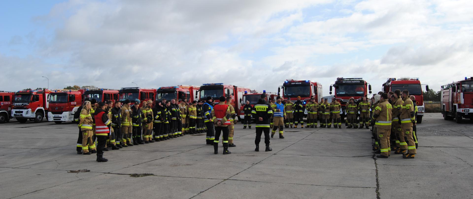Odprawa przed ćwiczeniami strażacy ustawieni w literę U słuchają dowódcy JRG przedstawiającego założenia do ćwiczeń