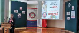scena na której jest ekran, baner i tablice tematyczne Obchody Światowego Dnia AIDS, na mównicy przemawia kobieta