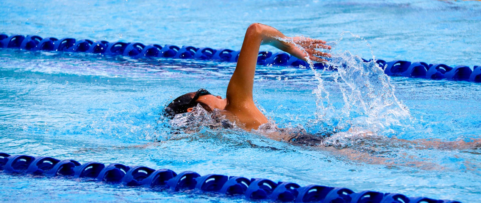 Młody zawodnik płynie po torze na basenie kraulem.
