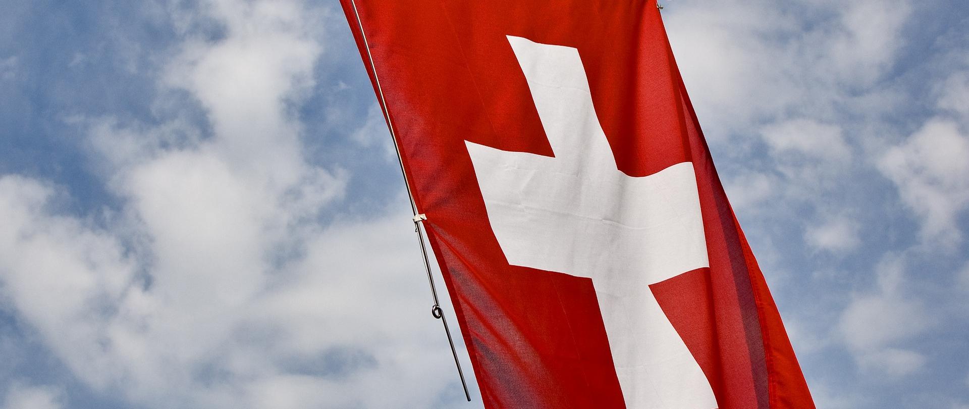 Zdjęcie ilustracyjne w poziomie. Flaga Szwajcarii na tle nieba