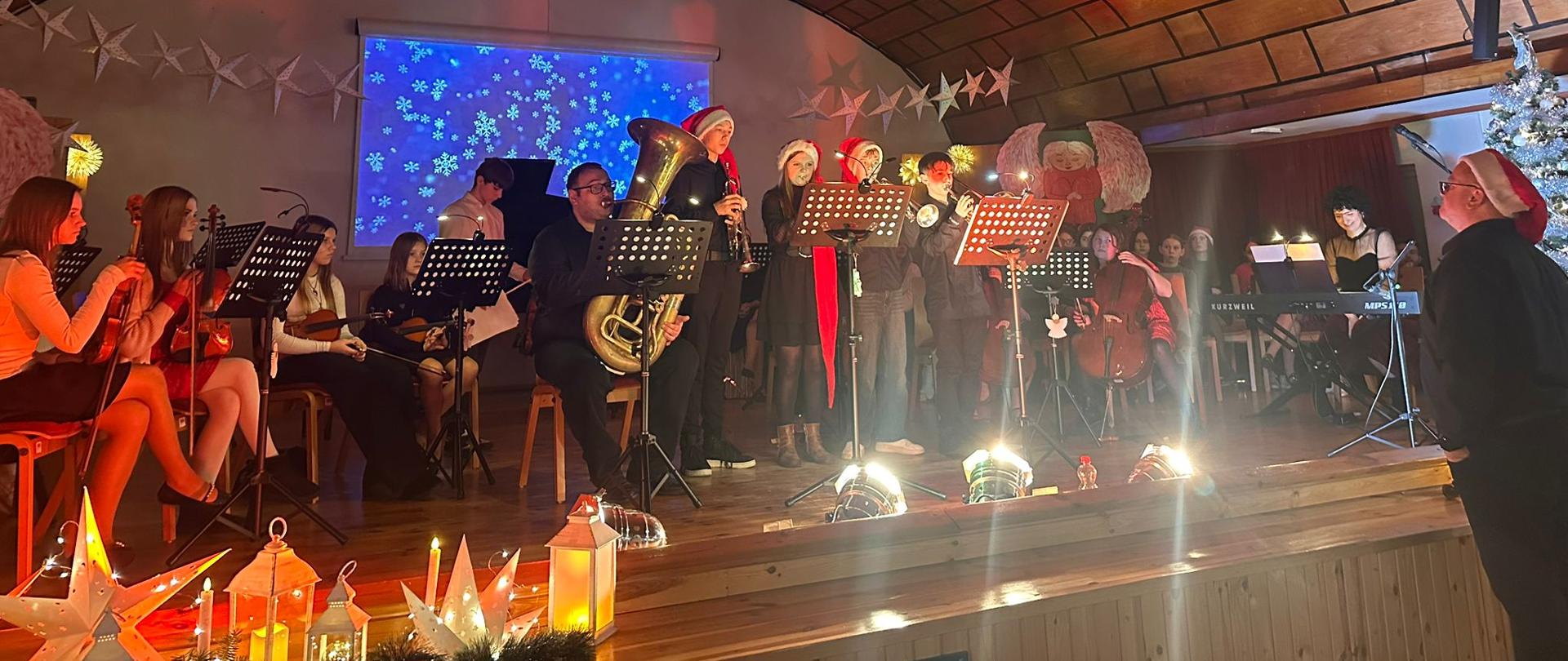 Muzycy w świątecznych strojach grają koncert na scenie szkolnej.