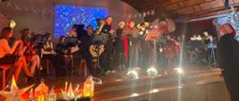 Muzycy w świątecznych strojach grają koncert na scenie szkolnej.